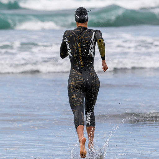 female running into the water wearing  Wikiwiki 3.0 Wetsuit - Gold 